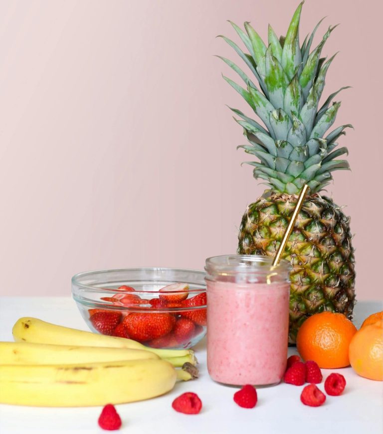 Ein Glas Erdbeersmoothie, Ananas, Bananen, Erdbeeren und Orangen auf einem Tisch.