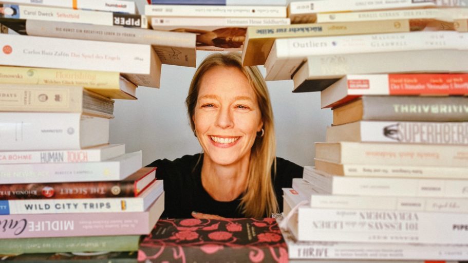 Bücher sind mein Leben. Lächelnde Frau zwischen Stapeln von Büchern, Hintergrund hell und schlicht.