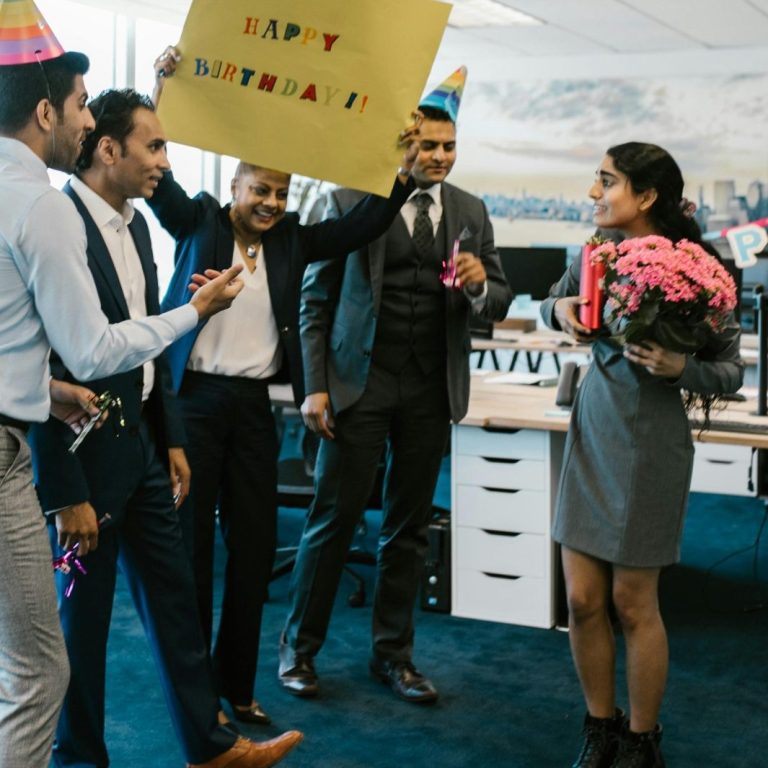 Feiernde Kollegen überraschen einen Mitarbeiter zum Geburtstag mit Geschenken und Jubel.
