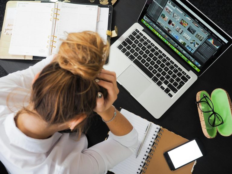 Eine Person mit zusammengebundenem Haar sitzt am Schreibtisch und betrachtet einen Laptop.