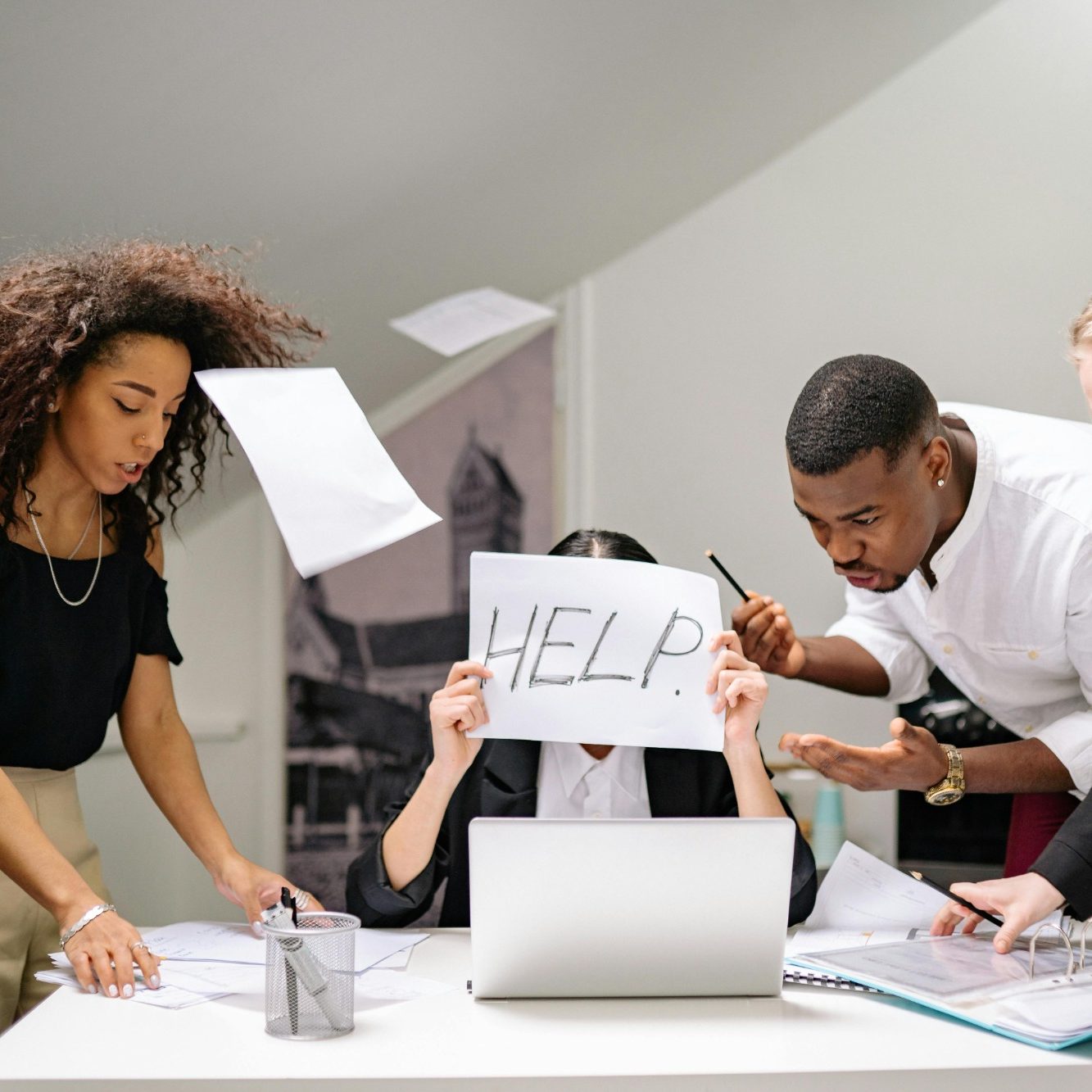 Besorgte Menschen um einen Tisch, eine Person hält ein "HELP"-Schild hoch.