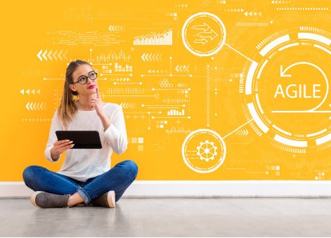 Frau mit Tablet sitzt vor einer gelben Wand mit "Agile"-Grafik.